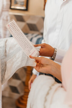 Close-up of hands holding a white embroidered baptismal towel (kryzhma) with a cross and dove, and a priest holding a prayer card during the ceremony.