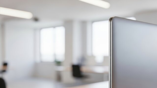 A close-up of a laptop corner against a blurred, bright office background.