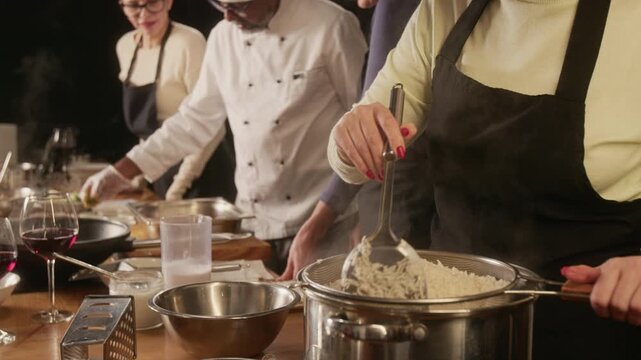 Tilt down shot of woman stirring rice in pan while chef and other women preparing meat during cooking master class in restaurant