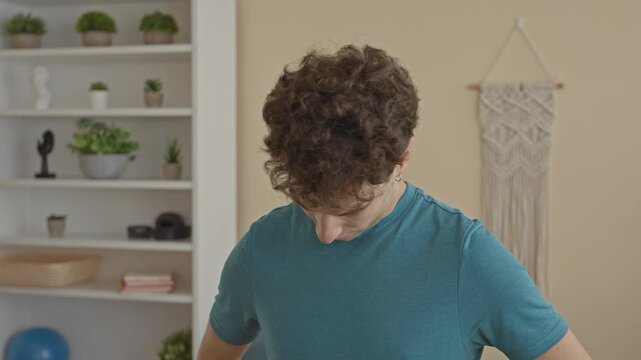 Man tilting head and stretching neck in a home studio with plants and macrame wall hanging; calm concentration.