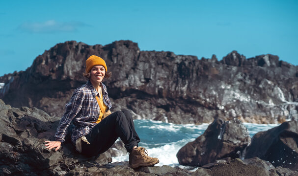 A girl is travelling, siiting by the Atlantic ocean on a rocks.