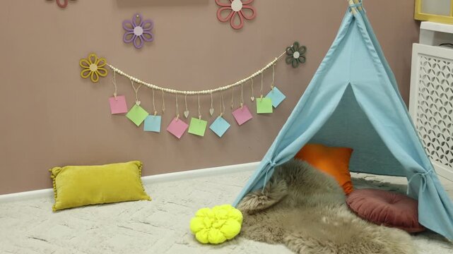 Colorful paper notes and beautiful decor hanging on beige wall near toy wigwam in stylish children's room, camera moving forward. Interior design