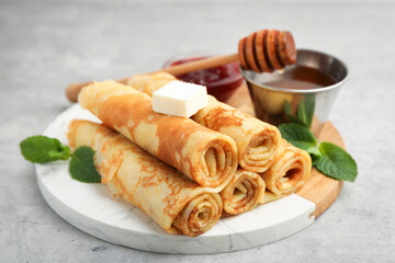 Tasty rolled crepes with honey, jam, butter and mint leaves served on light grey table, closeup © New Africa