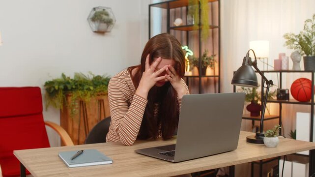 Young woman at home works on laptop reads game loss and failed bet notice and sighs feels upset and low. Caucasian girl at table looks down frowns and pauses typing tries to calm mood and accept news