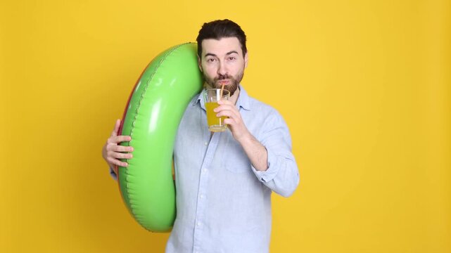 Handsome man in beachwear with cocktail and inflatable ring on orange background