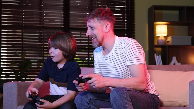 Happy father and son with controllers playing video game on sofa at home