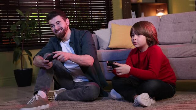 Emotional father and son with controllers playing video game at home