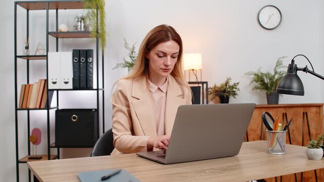 Middle-aged businesswoman at home office opens laptop smiles and starts typing first tasks of day with energy. Freelancer girl at table writes plan answers email drafts and gets ready to work day