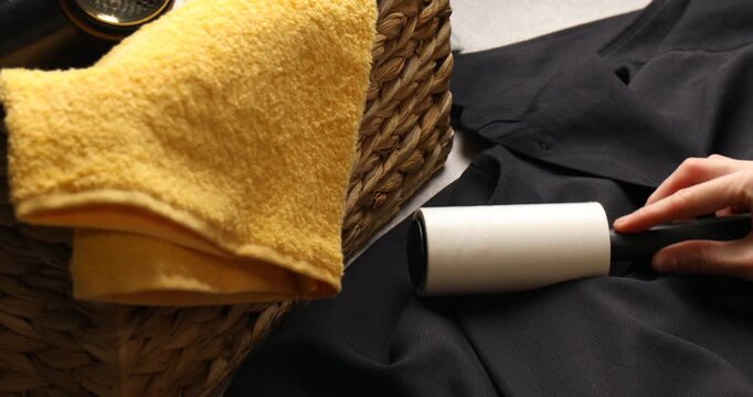 Woman cleaning jacket with lint roller at table indoors, closeup
