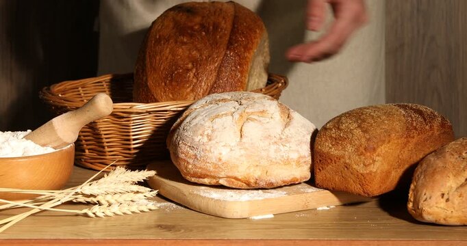 Woman putting different types of bread into wicker basket at wooden table, closeup