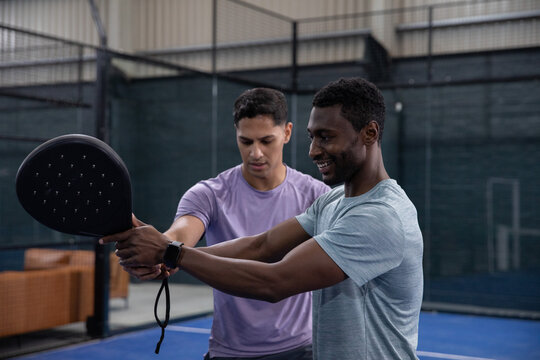 Coaching coach guiding trainee in athletic shirts on blue court, showing paddle grip and smartwatch