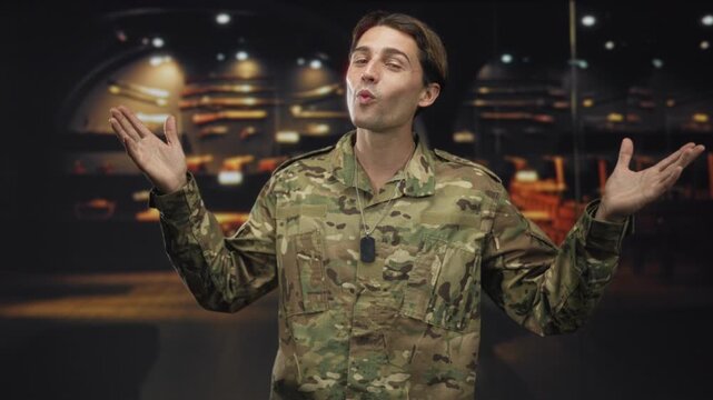 Man soldier in camouflage with dog tag and hands raised palms up, shrugging in a building beside rifle display under spotlights; pride duty.