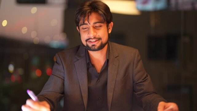 Assertive Indian software architect preparing comprehensive technical strategies overlooking a vibrant metropolitan night scene inside a sophisticated executive workspace.