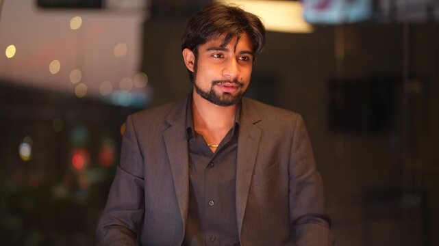 Poised South Asian IT director supervising cross border tech operations overlooking a vibrant metropolitan night scene inside a sophisticated executive workspace.