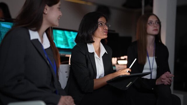 Trio of multicultural software experts comprising asian, european, and american women reviewing analytical dashboards and system logs at a state of the art data control center hub.