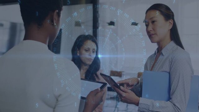 Three businesswomen collaborating in glass office, left woman tapping tablet, HUD overlay appearing