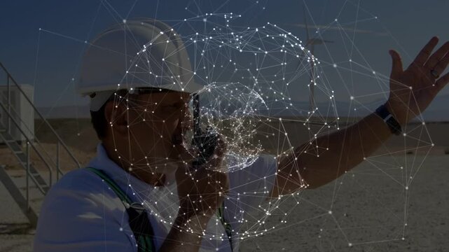 Site worker speaking into radio and pointing, coordinating turbine work with pulsing network sphere