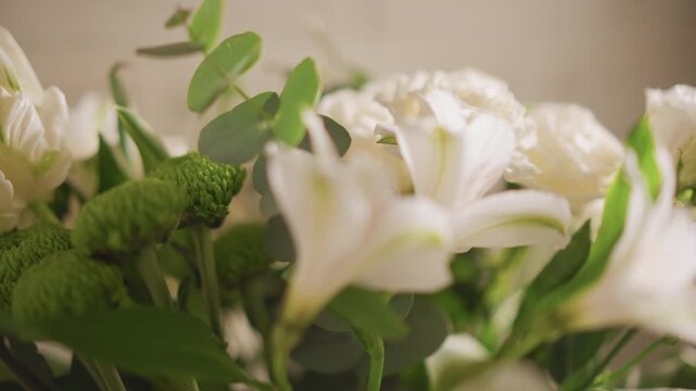 White floral bouquet on home table, soft morning light, closeup of lilies and roses with eucalyptus and green chrysanthemums, shallow depth of field, warm neutral background, delicate petals,