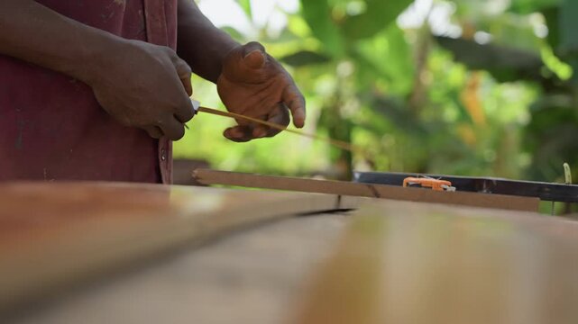 Closeup black hands aligning wooden boards outdoors with ruler and clamp, measuring spacing for deck installation, green garden backdrop, sawdust flecks, steady practical construction process, focused