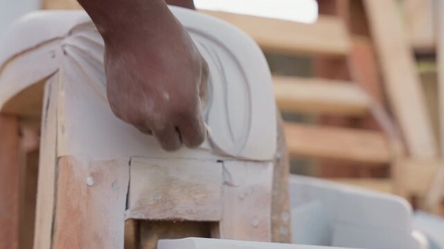 Worker hands carving wooden decorative molding in busy furniture workshop, active shaping and sanding, assemblyready ornament for cabinet or chair, focused technique and industrial backdrop