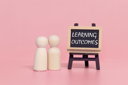 Two wooden figures standing next to learning outcomes chalkboard