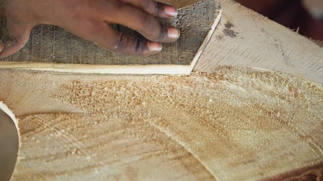 Close up hands smoothing wood surface, finish carpentry inspection and polishing craftsman or furnituremaker using fine abrasive to refine edge, checking grain and sheen, buffing to satin finish,