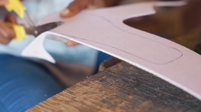 Closeup hands cutting template on workbench. Quiet artisan carpentry scene with scissors trimming curved pattern from thin plywood template on rough wooden bench, fingers guiding precise cut, small