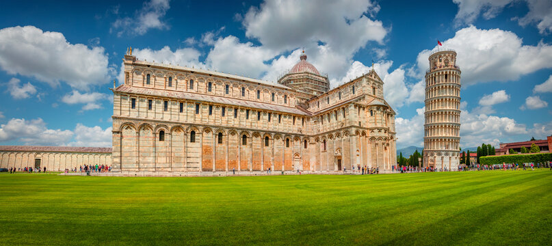 Panoramic summer view of famous Leaning Tower in Pisa. Bright evening scene with hundreds of tourists in Piazza dei Miracoli (Square of Miracles), Italy, Europe. Traveling concept background.