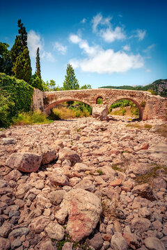 Vertical summer view of Roman bridge across the Torrent de Sant Jordi river. Colorful afternoon scene of Pollenca cityscape, Majorca, Balearic islands, Spain, Europe. Traveling concept background.