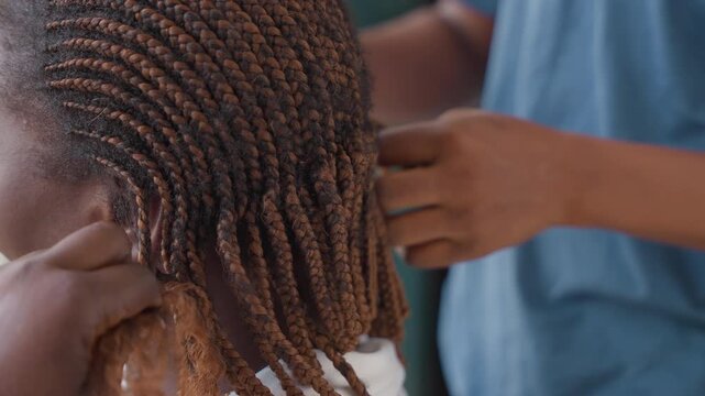 Black hairstylist braiding natural textured hair, closeup hands twisting neat rows, focused stylist in blue shirt, gentle touch conveying care and tradition in intimate home setting