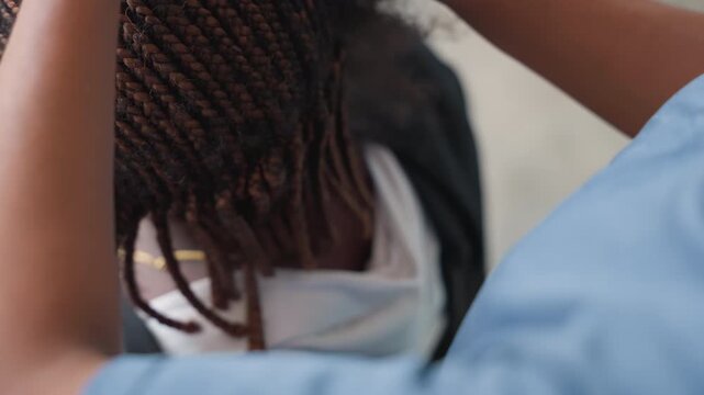 Closeup assistant adjusting braided hair near neckline, uniformed helper checking alignment and symmetry, gentle fingers tucking ends and securing with clasp, routine salon appointment vibe, focused