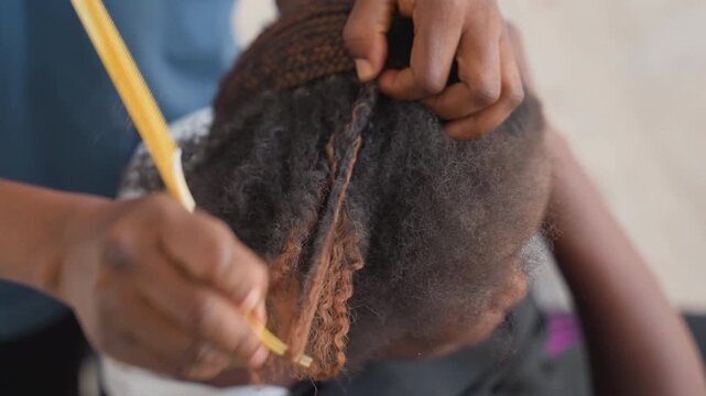 Closeup hands braiding childs hair, stylist using crochet hook to interlock colored extension into cornrows, patient precise technique, textured natural hair, intimate home salon atmosphere, caring