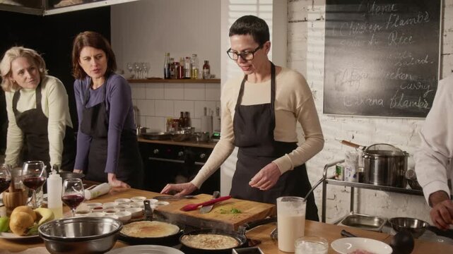 Biracial chef teaching group of three women how to cook crepes during cooking master class in restaurant