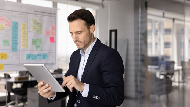 Virtual project management. Focused busy mid adult male business specialist work on digital pad in office manage tasks in online planning app use ai to check risks create ideas set goals for sprints