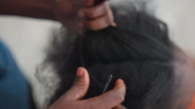 Closeup hands detangling natural hair, gentle athome sequence showing patient fingers separating knots using comb and elastic to smooth textured afro, soft light and warm domestic atmosphere, focus