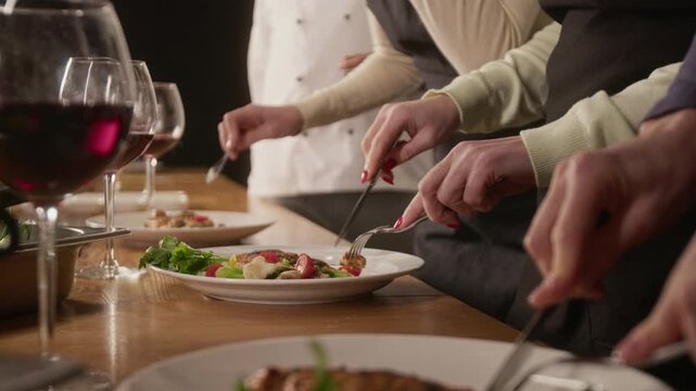 Low angle close up shot of group unrecognizable hands carving roasted meat and with side of vegetables and herbs on plate