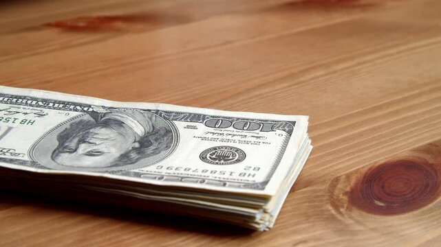 Stacks of fresh cash are carefully arranged on a smooth wooden table, creating a beautiful contrast. Hand movements add life to the scene, hinting at plans ahead