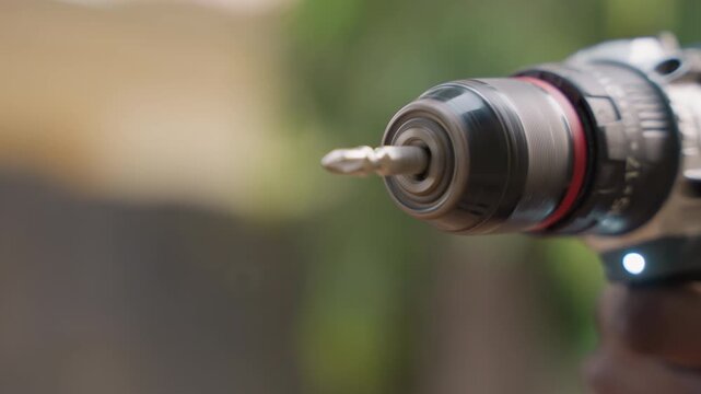 Closeup of woodworker drill bit poised, shallow depth of field with blurred greenery, rotating metal bit and rugged chuck in focus, ready to engage timber, dynamic carpentry action and confident
