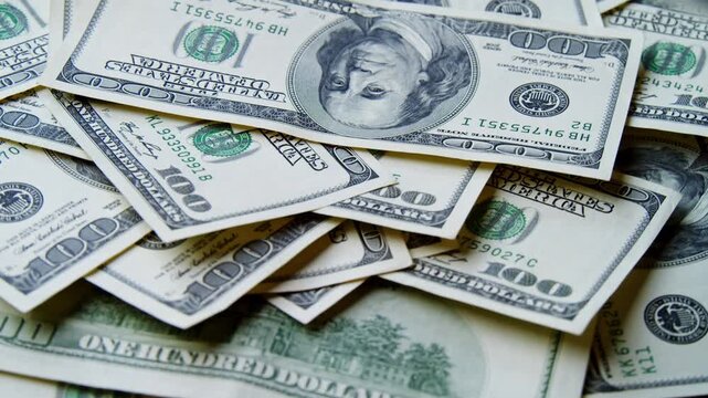 Crisp hundred dollar bills lay scattered across a table, showcasing their vibrant colors and detailed designs under warm sunlight, creating a mesmerizing pattern