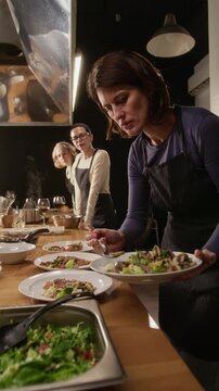 Vertical low angle shot of woman adding vegetables to dishes, finishing cooking master class in restaurant
