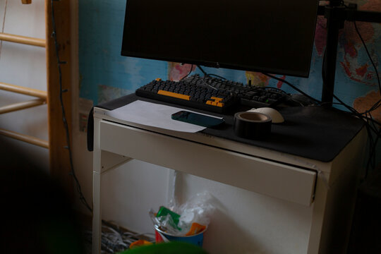 Busy study desk interior with keyboard, scattered wrappers and bag under desk, monitor glowing against map wallpaper, latenight study vibe and casual organization.