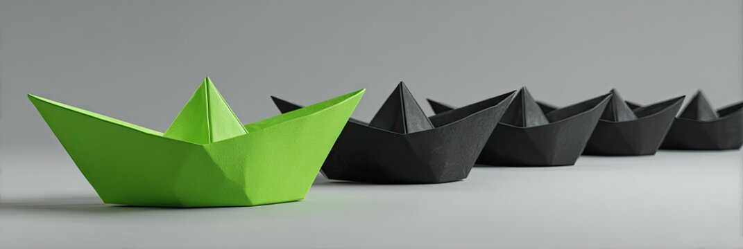 Group of paper boats, one green leads several black boats on a light gray surface