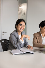 Portrait of smiling businesswoman, professional team member sitting at table with laptop, participating in corporate meeting with business colleague, looks at camera, represents success and leadership