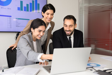 Smiling multiethnic business team engaged in successful collaboration, review data on laptop, discussing sales statistics during office meeting in boardroom. Financial analysis, strategy development