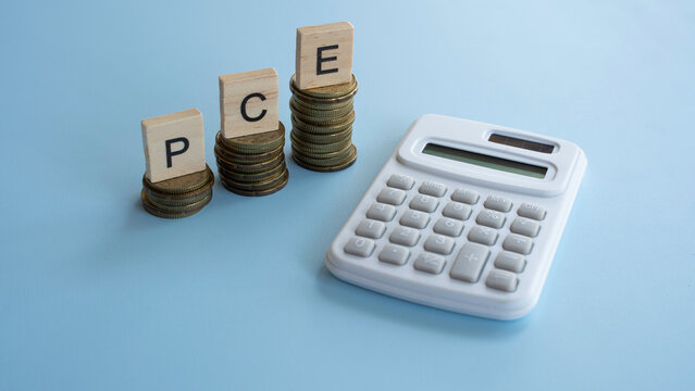 PCE letters on wooden blocks with gold coins and a calculator for personal consumption expenditures and economic inflation tracking.