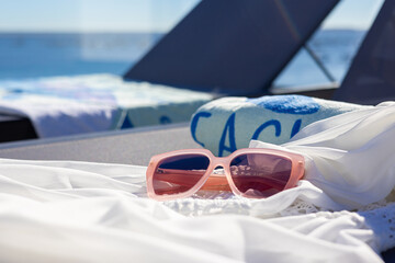 Plakat Close up of pink sunglasses on white dress on sunbed with sea view creating relaxing summer vacation mood
