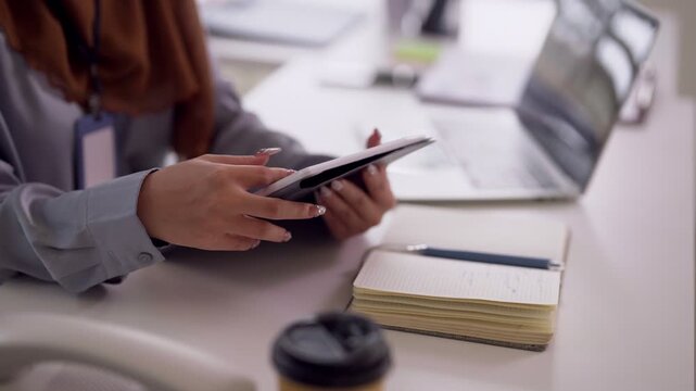 Adult Asian businesswoman using digital tablet for remote work at modern office desk boosting productivity