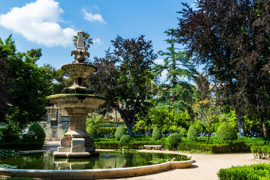 Stone fountain in landscaped garden with trees and trimmed bushes