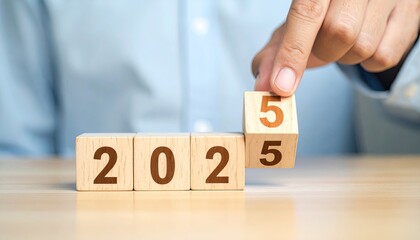 Naklejka premium Hand placing a block on wooden blocks that spell out the year 2025 on a table