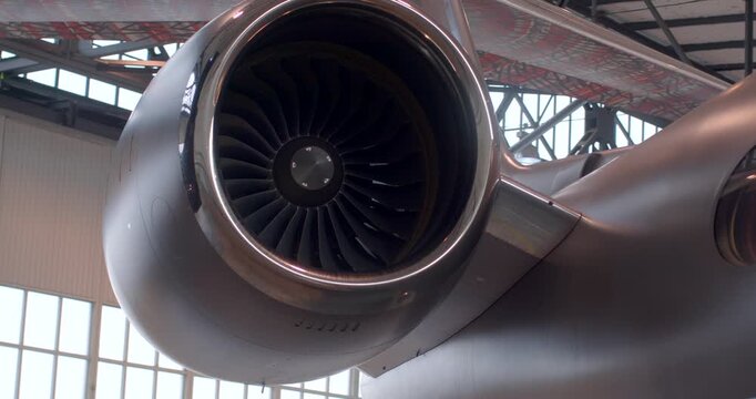 Silver aircraft jet engine nacelle, closeup view of polished intake and fan blades in hangar environment with implied engineer inspection and precision maintenance atmosphere
